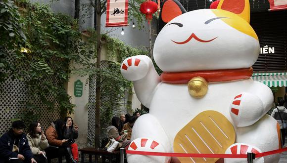 This photograph taken on January 17, 2023 shows people eating ice cream next to a large cat statue at an ice cream shop in Hanoi, ahead of the lunar new year. - As China gears up to welcome the Year of the Rabbit, the lunar new year looks slightly different in Vietnam -- where the Year of the Cat is about to begin. (Photo by Nhac NGUYEN / AFP)