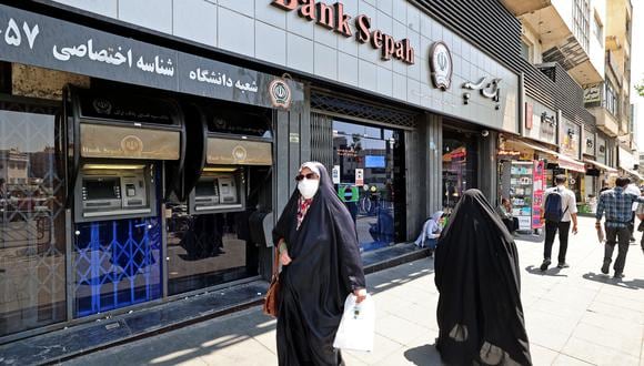 Una mujer iraní con una mascarilla pasa frente a una sucursal cerrada de Bank Sepah en el centro de Teherán el 20 de julio de 2021.  (Foto de ATTA KENARE / AFP)