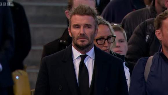 David Beckham, de 47 años, fue descubierto por la prensa mientras esperaba en la fila, vestido con traje, corbata y abrigo negros.  (Foto: captura YouTube)