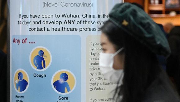 En el Aeropuerto de Heathrow, una mujer con una máscara facial pasa un letrero de Salud Pública de Inglaterra, advirtiendo a los pasajeros que llegan en vuelos al Reino Unido, que un virus ha sido detectado en Wuhan, China. (AFP)