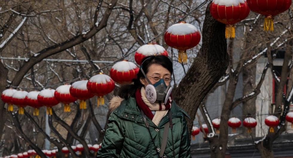 Una mujer que usa una máscara protectora para prevenir la propagación del coronavirus camina por una calle después de una nevada en Beijing. (AFP)