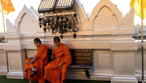 Los monjes budistas revisan sus teléfonos en el templo Wat Saket mientras se pone el sol en Bangkok el 9 de noviembre de 2021. (Foto de Jack TAYLOR / AFP)