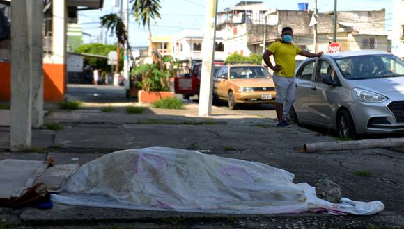 A man looks at a body said to be laying for three days oustide a clinic in Guayaquil, Ecuador on April 3, 2020. - Troops and police in Ecuador have collected at least 150 bodies from streets and homes in the country's most populous city Guayaquil amid warnings that as many as 3,500 people could die of the COVID-19 coronavirus in the city and surrounding province in the coming months. (Photo by Str / Marcos Pin / AFP)
