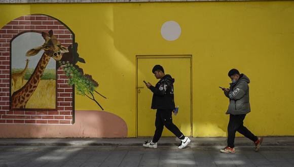 Personas que usan su teléfono caminan por una calle en Beijing el 2 de diciembre de 2021. (Foto de Jade GAO / AFP)