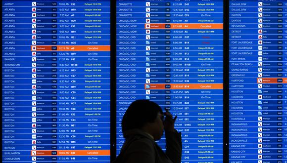Los viajeros miran una pantalla de información de vuelos que enumera los vuelos cancelados y retrasados ​​debido a una interrupción de la FAA que dejó en tierra los vuelos en los EE. UU. En el Aeropuerto Nacional Ronald Reagan de Washington en Arlington, Virginia, el 11 de enero de 2023. (Foto de SAUL LOEB / AFP)