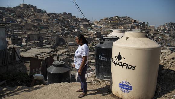 Griselda posa para una foto junto a tambores de agua fuera de su casa mientras espera que llegue un camión cisterna para poder comprar agua potable, en Pamplona Alta, en las afueras del sur de Lima, tomada el 22 de marzo de 2022, en el Día Mundial del Agua. (Foto de Ernesto BENAVIDES / AFP)