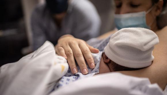 Imagen referencial. Un padre y una madre miran a su hijo recién nacido durante la pandemia de coronavirus, 17 de noviembre de 2020. (Martin BUREAU / AFP).