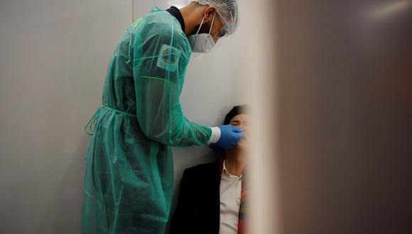 Un trabajador de la salud toma un hisopo de un pasajero de un vuelo desde China en las cabinas de prueba de COVID-19. (Foto por JULIEN DE ROSA / AFP)