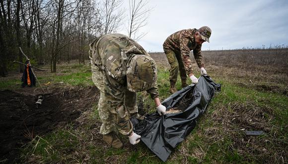 Miembros del equipo de Cooperación Civil-Militar de Ucrania colocan en una bolsa de plástico el cuerpo de un soldado en el norte de la región de Kharkiv el 11 de abril de 2023, en medio de la invasión rusa de Ucrania (Foto de SERGEY BOBOK / AFP)